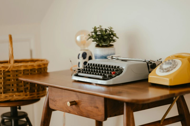un tavolino da ingresso con una macchina da scrivere olivetti, un telefono a disco e alcune piantine
